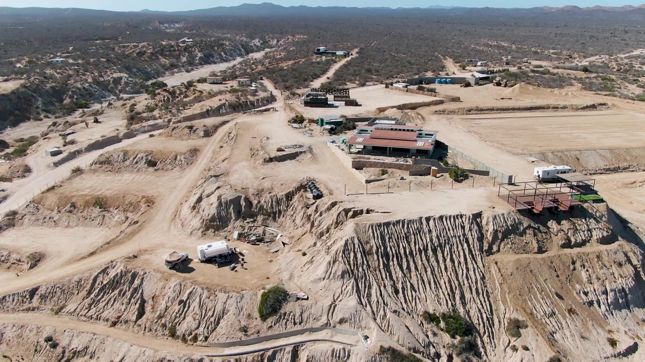 Drone view in La Fortuna, Baja California Sur, looking across graded dirt roads, a large excavated slope, scattered vehicles, small site structures, and no visible people.