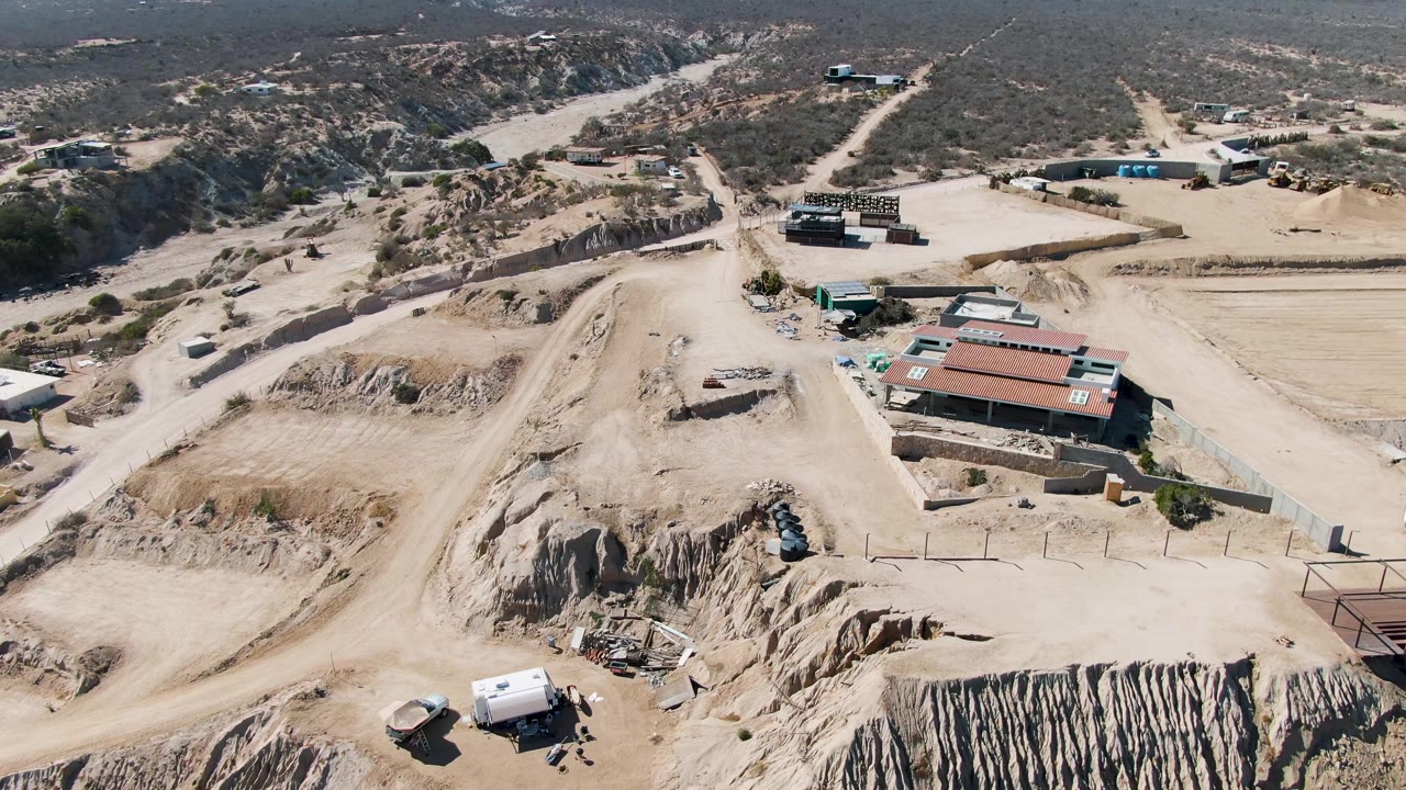 High aerial view of desert excavation site with roadways, buildings, and parked vehicles