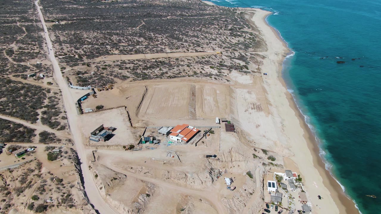 High aerial view of road, construction site, beach, and ocean waves.