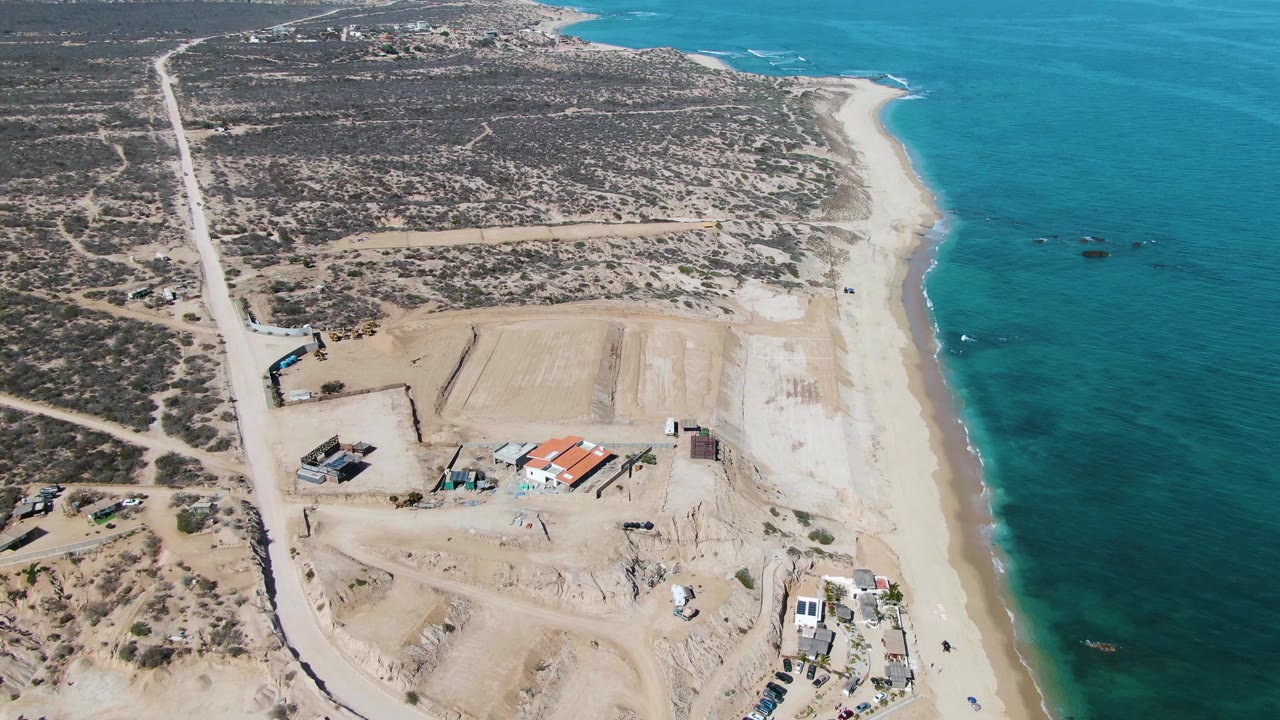 Drone view of beach, blue water, scrubland roads, and cleared sand lots.