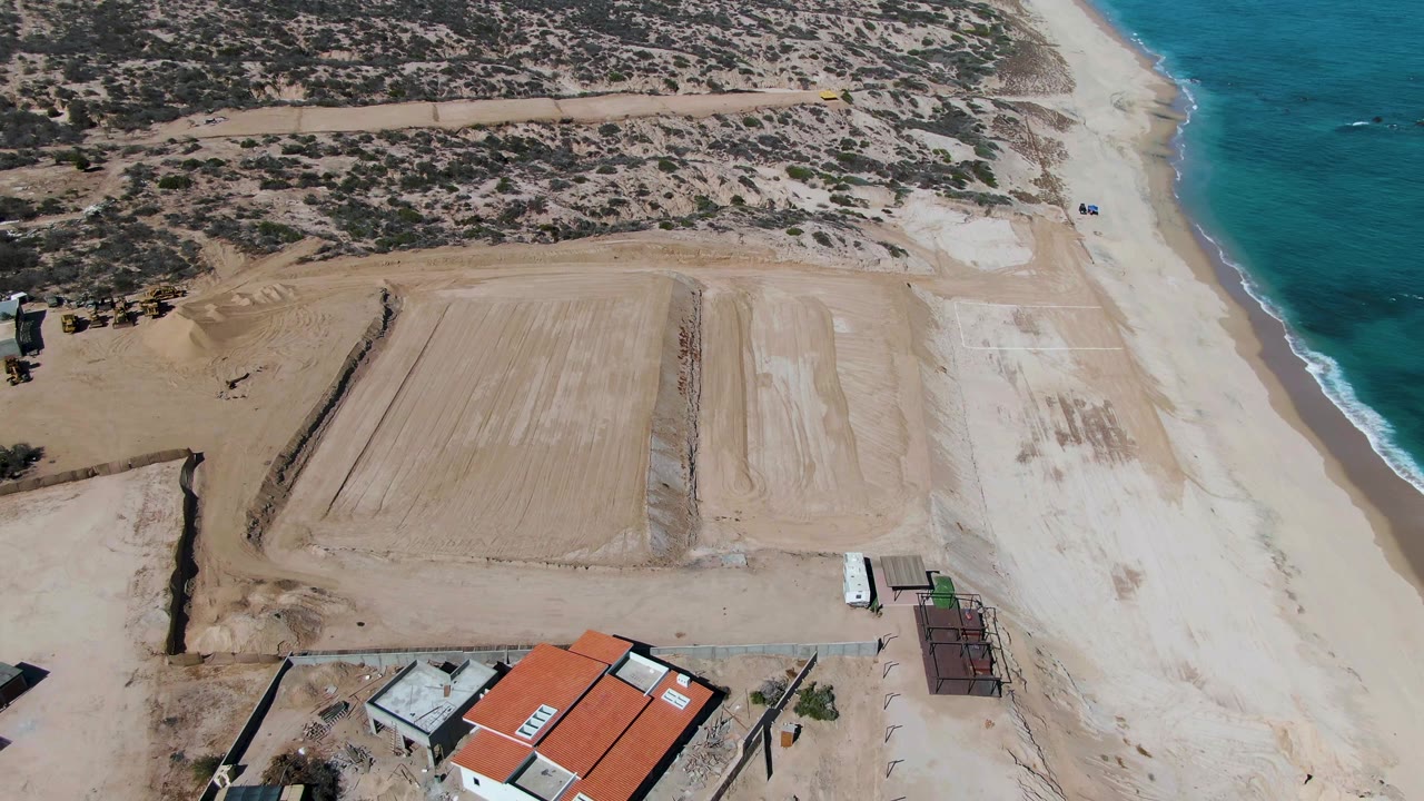 Overhead coastal construction site with beach and ocean to the right.