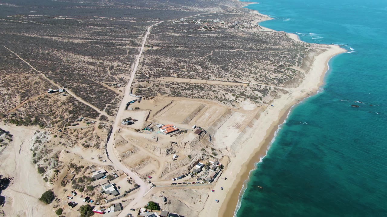 Aerial coastline view with turquoise water, pale beach, desert roads, and graded construction.