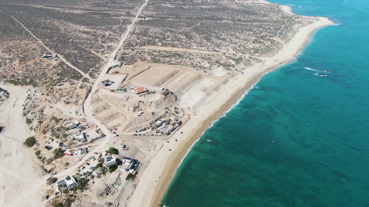 Drone view of dirt roads and construction lots along a sandy coast.