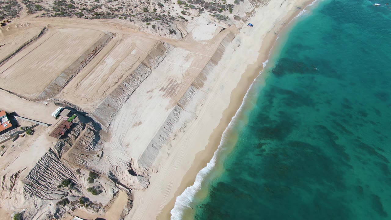 Aerial view of sand piles beside a turquoise shoreline
