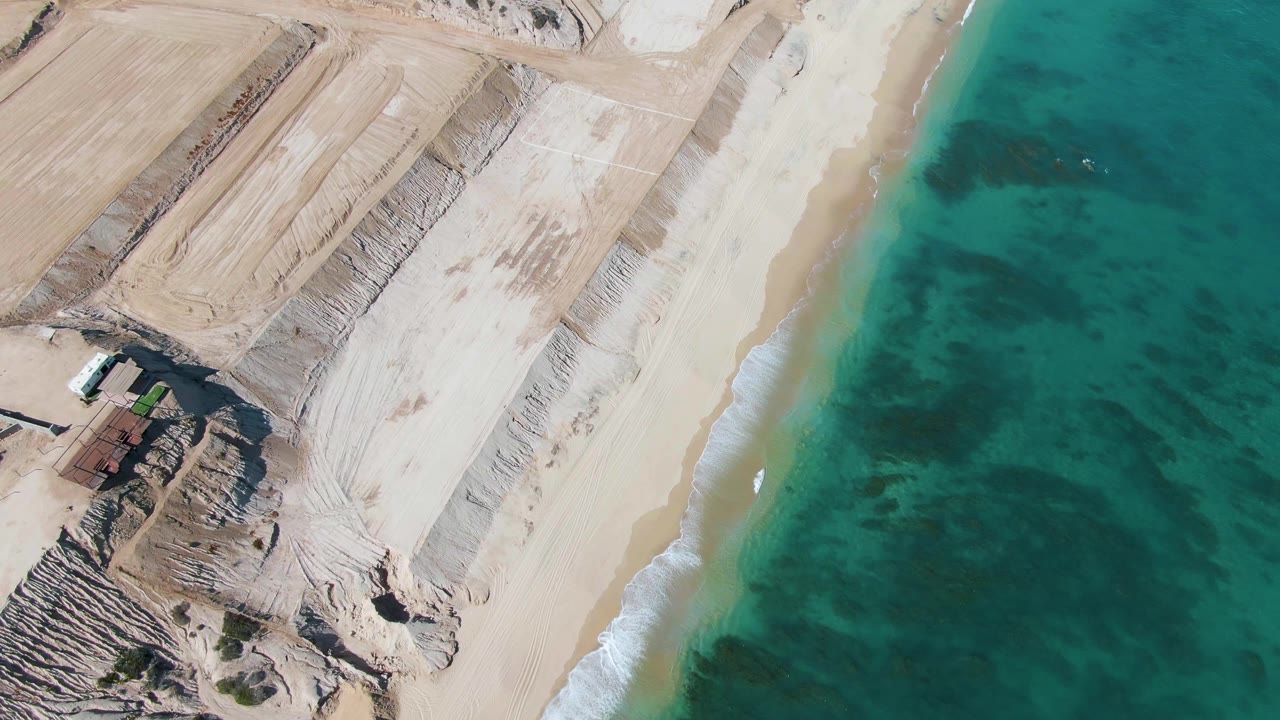 At three seconds, the frame looks down on terraced sand forms, an empty bright beach, a thin line of foam, turquoise ocean, and no visible people in La Fortuna.