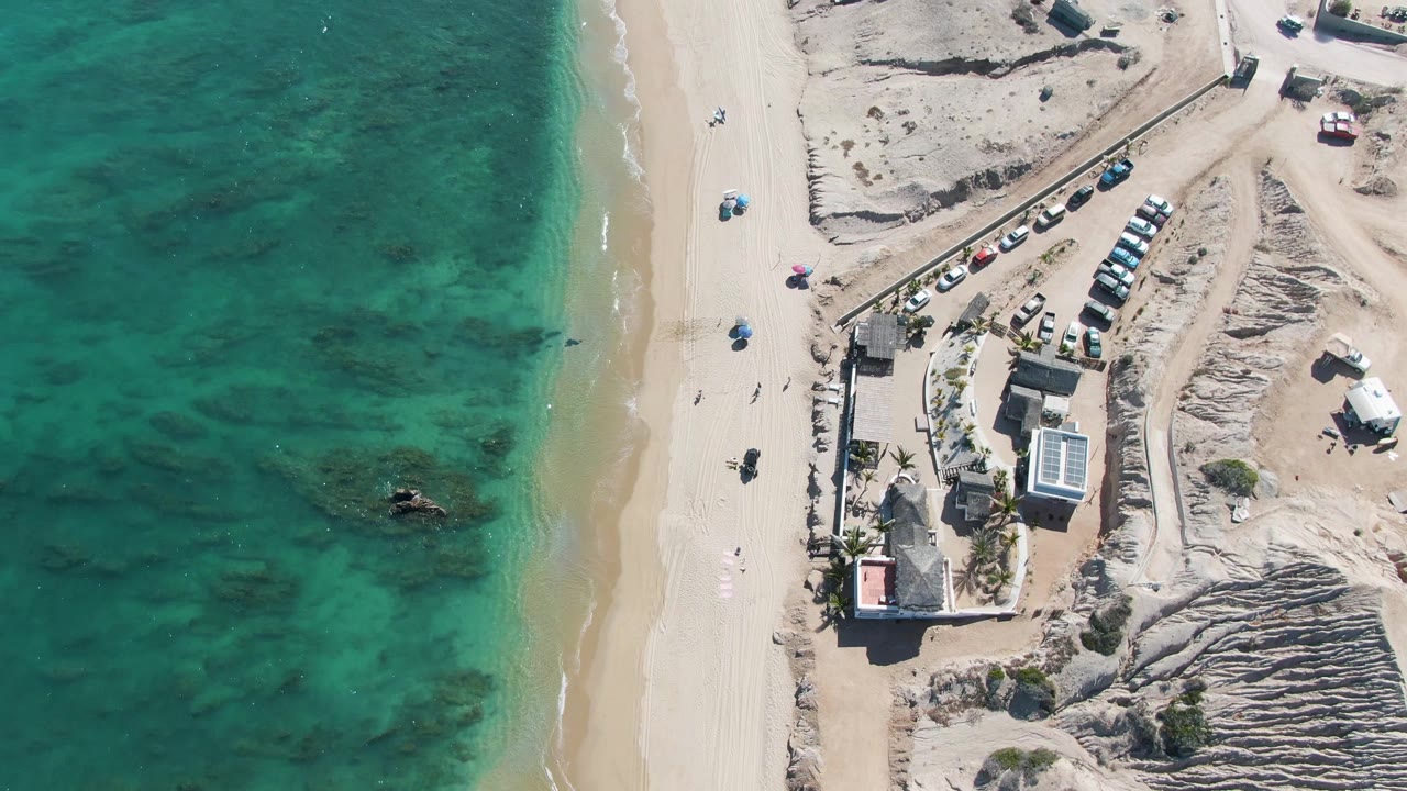 Top-down coastline with turquoise water and parking lot near buildings
