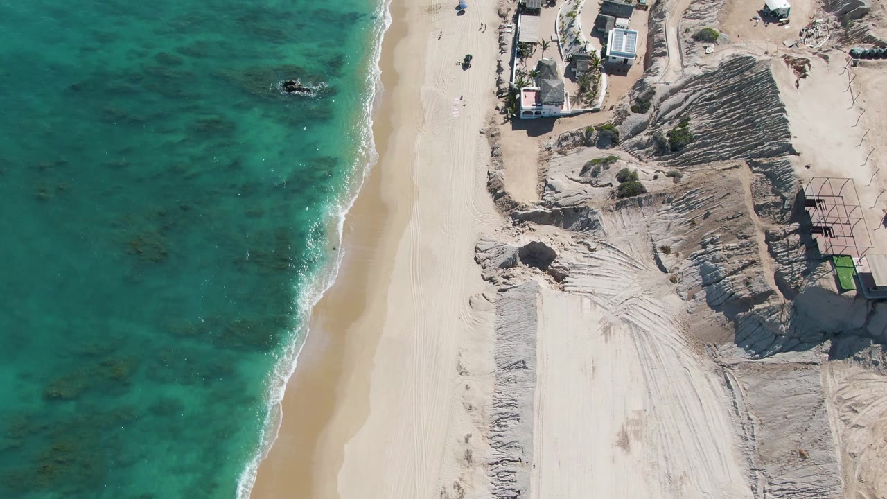 Top-down coastline with sandy path, vehicles, dunes, and surf
