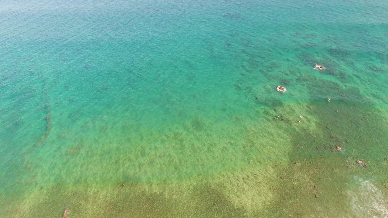 Overhead turquoise shallow water with visible seabed and submerged rocks.