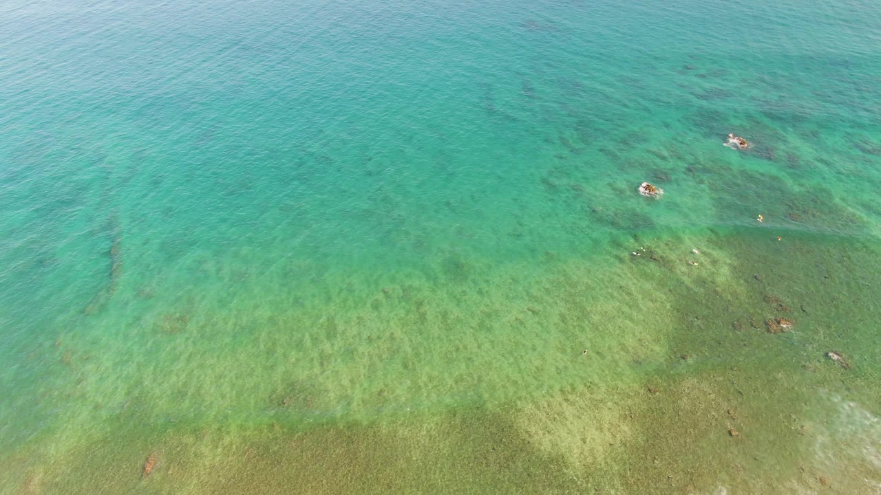 Turquoise overhead water at La Fortuna, Baja California Sur, with the seabed visible below, small rock clusters near the upper right, and no visible people.