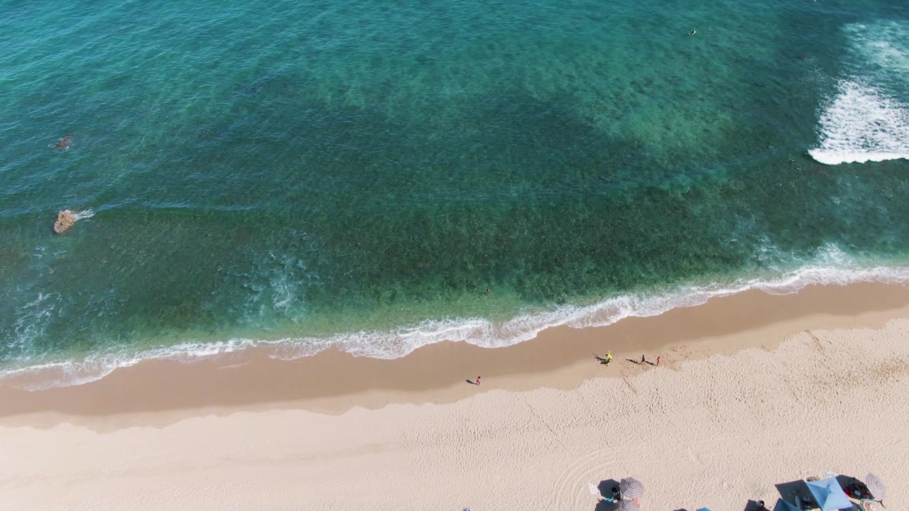 Turquoise ocean and sandy shore with small beachgoers near the waterline.