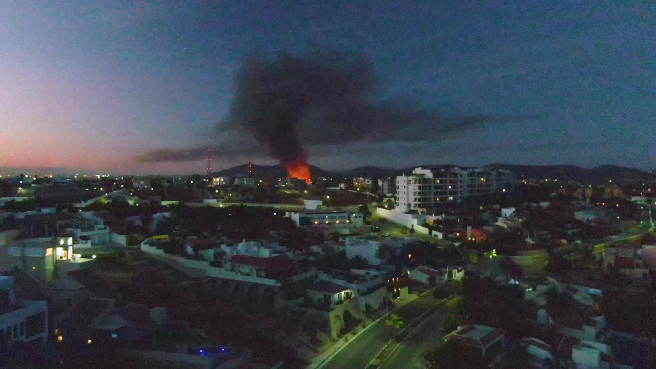 Aerial neighborhood view with orange fire and heavy smoke at dusk.