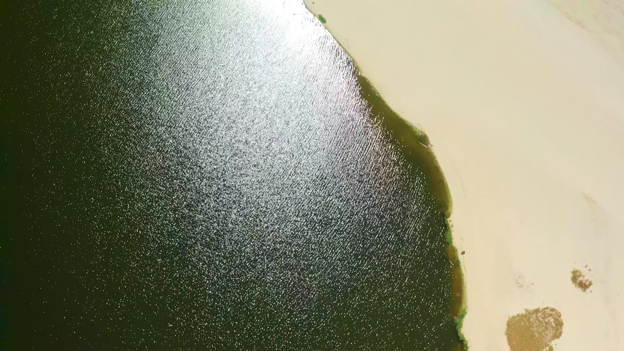 Dark green water beside pale sand with bright surface glare.
