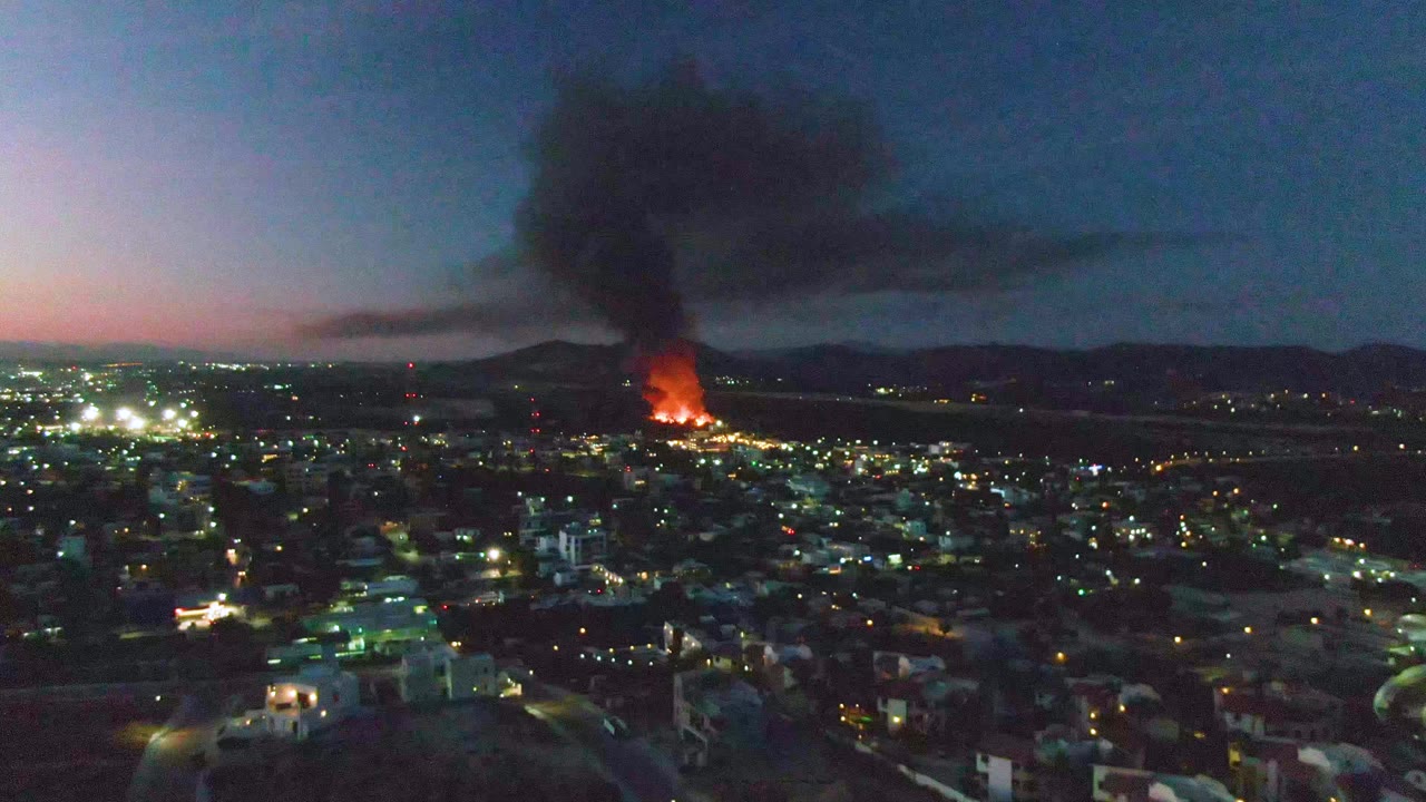 Distant fire burning beyond city buildings at dusk