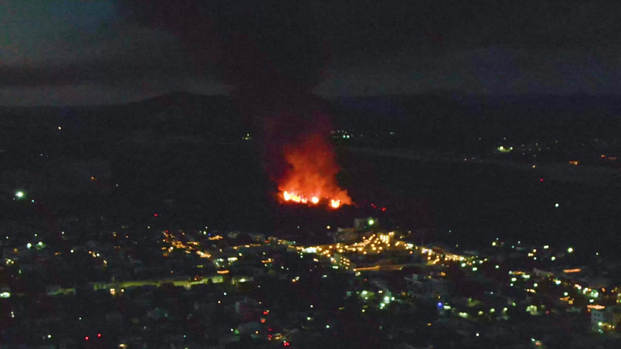 The fire glows strongly above the San Jose del Cabo street lights, with smoke thickening upward against the dark horizon and no visible people.