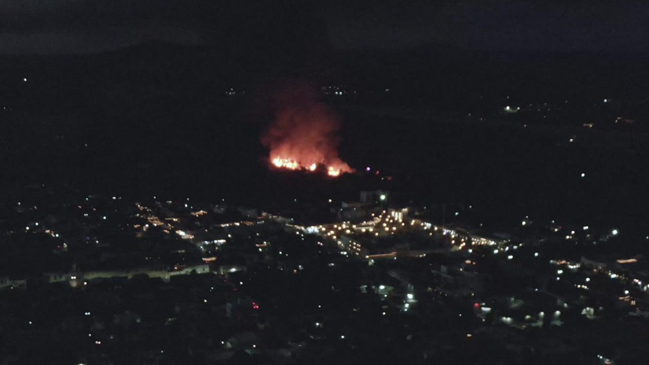 A nighttime aerial frame in San Jose Del Cabo shows a concentrated fire glow near the upper frame, city lights below, and no visible people.