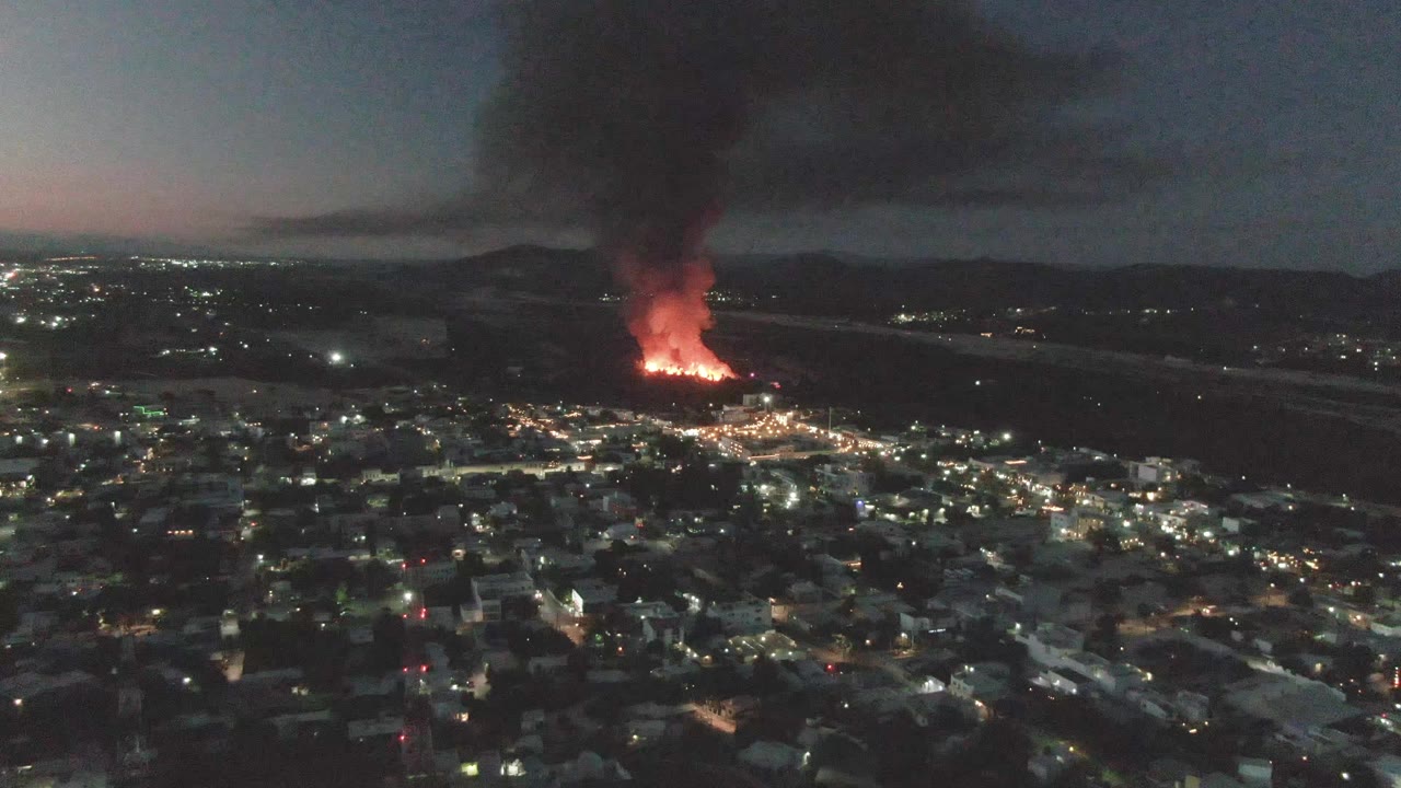 City lights below a distant orange fire with a dark smoke column.