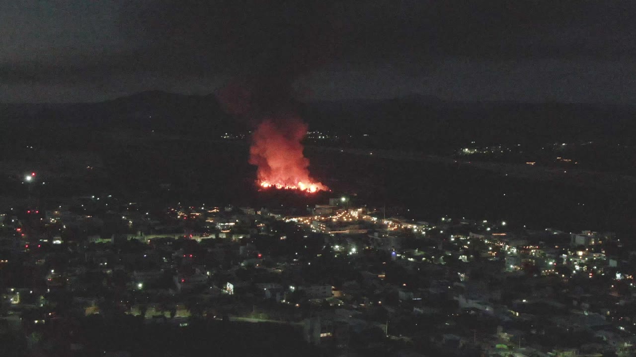 At 0:01, the red fire and smoke sit beyond the illuminated San Jose del Cabo urban area, with scattered lights below and no visible people.