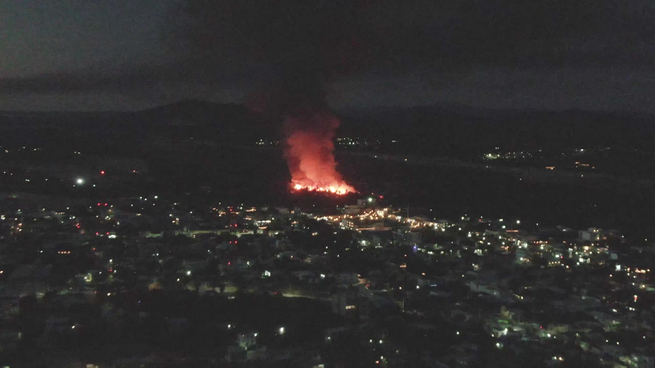 Night aerial city view with distant red fire and black smoke