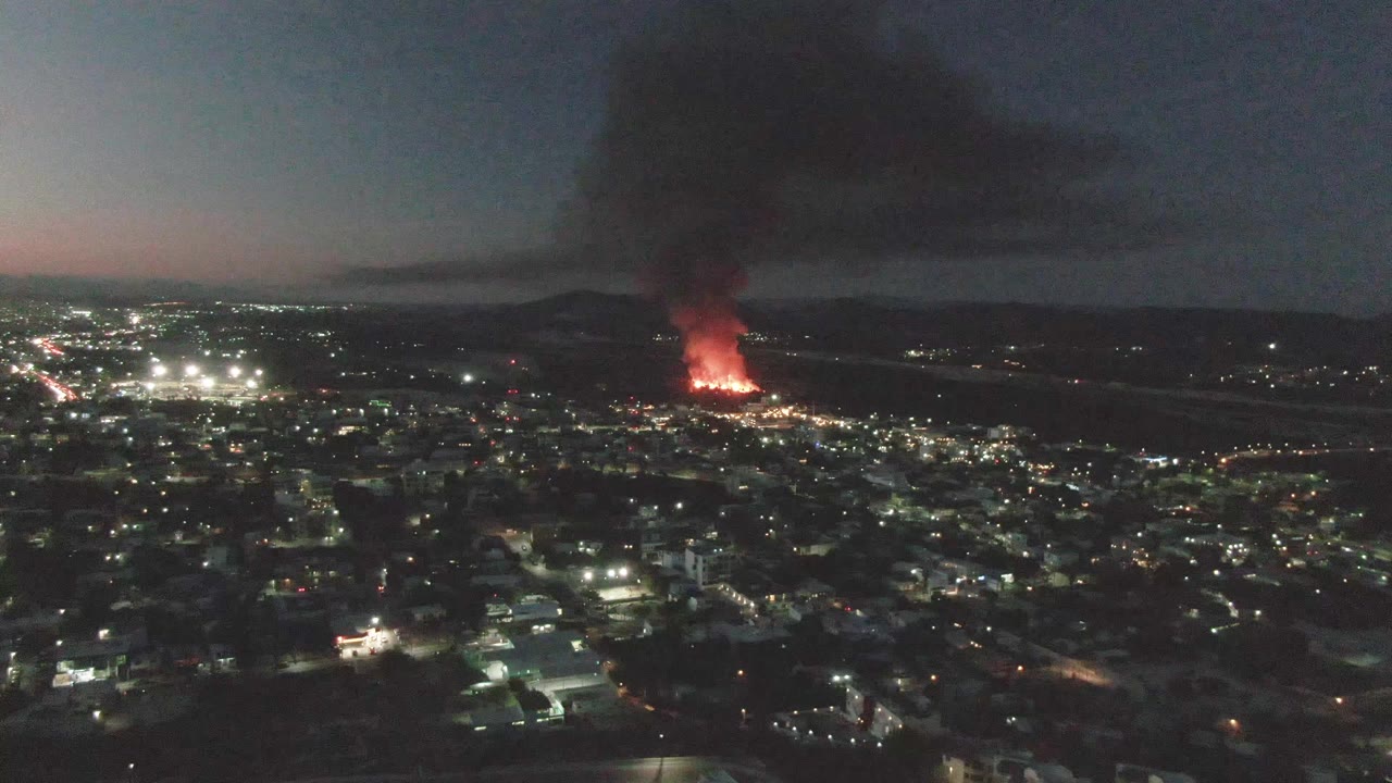 City lights at night with a large smoke plume from a distant fire.