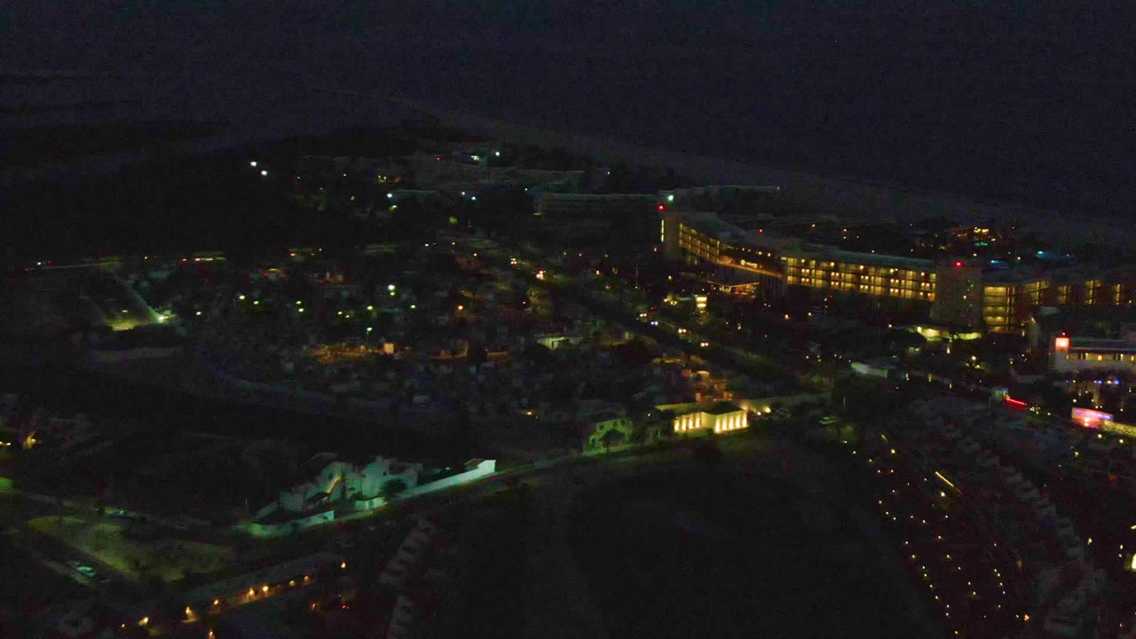 Dark aerial view of a coastal town with street lights and ocean horizon.