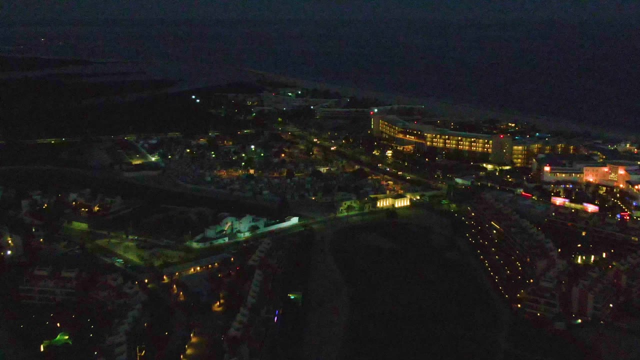 Mid-clip San Jose Del Cabo aerial frame with the sky slightly lighter, street lights tracing the roads, a large lit building near the center-right, and no visible people.