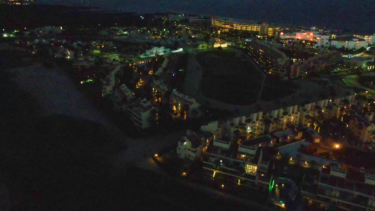 Aerial view of beachside buildings and town lights under a slightly brighter dawn sky.