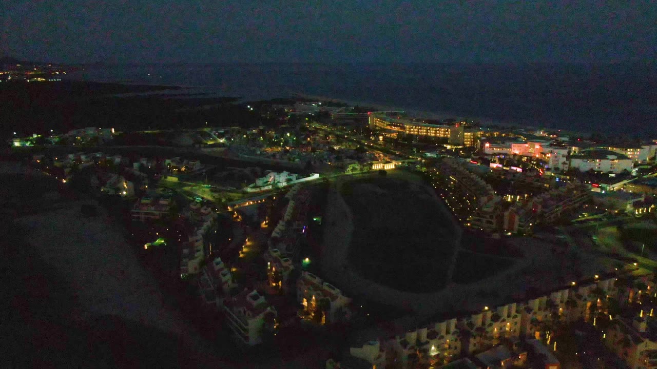 Aerial night view of coastal town with open field and lit streets.