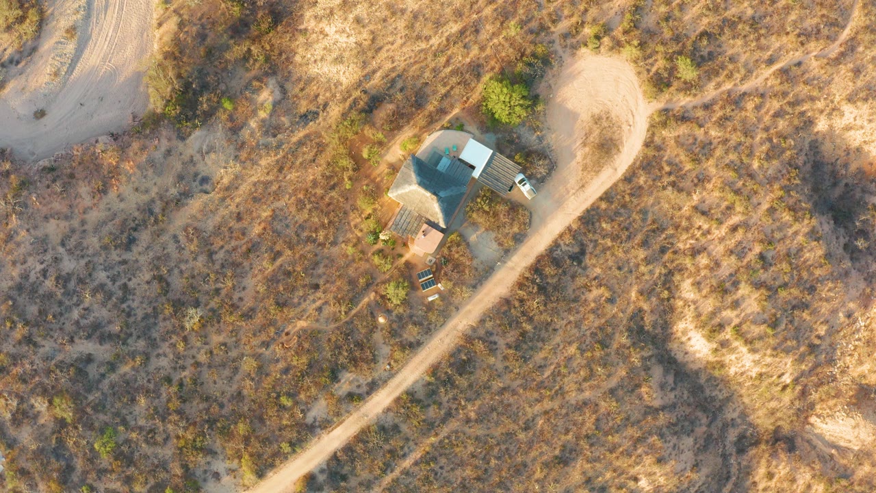 Small roofed structure and curving dirt road seen from above.