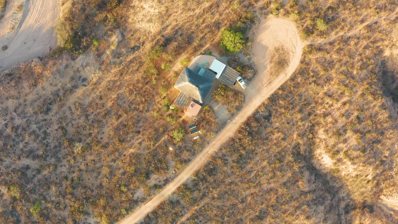 At 0:00, an overhead drone view in Cabo Pulmo, Baja California Sur shows a small house beside a pale dirt road, dry grass, scattered shrubs, and no visible people.