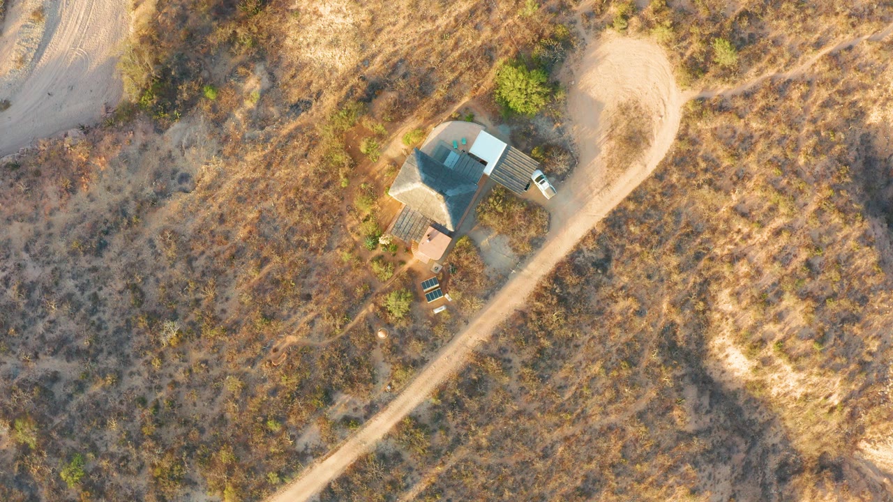 Aerial view of the house, curved dirt road, dry vegetation, and nearby white car.