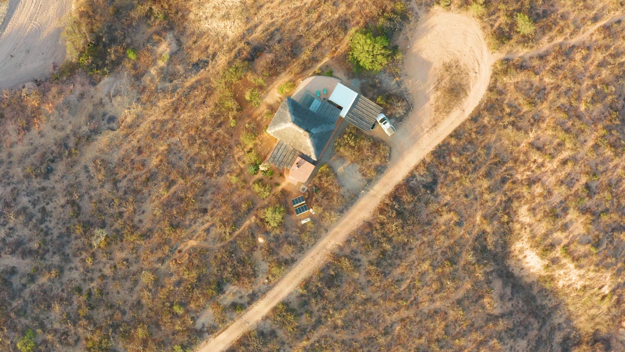 At 0:00, an overhead drone frame shows a small rural house near a curving dirt road in Cabo Pulmo, Baja California Sur, with a white vehicle nearby and no visible people.