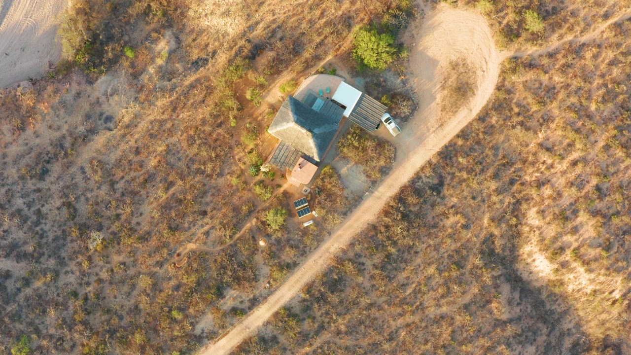 Aerial view of a white vehicle near a small house and dirt road.