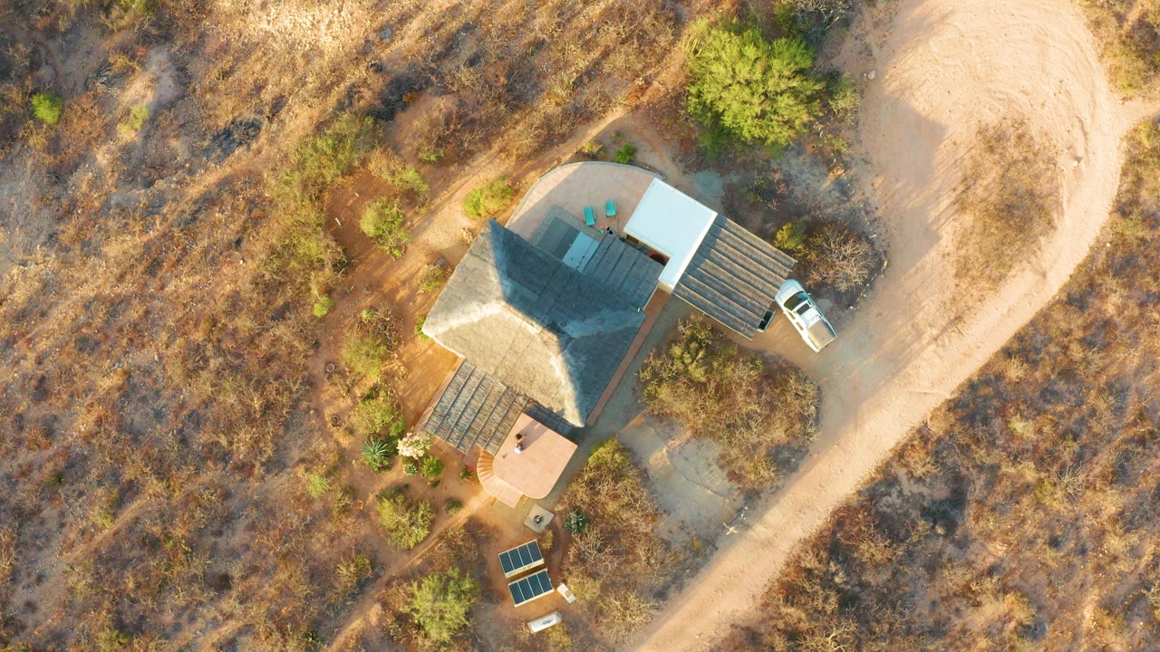 Drone view of a house in arid terrain with solar panels nearby.