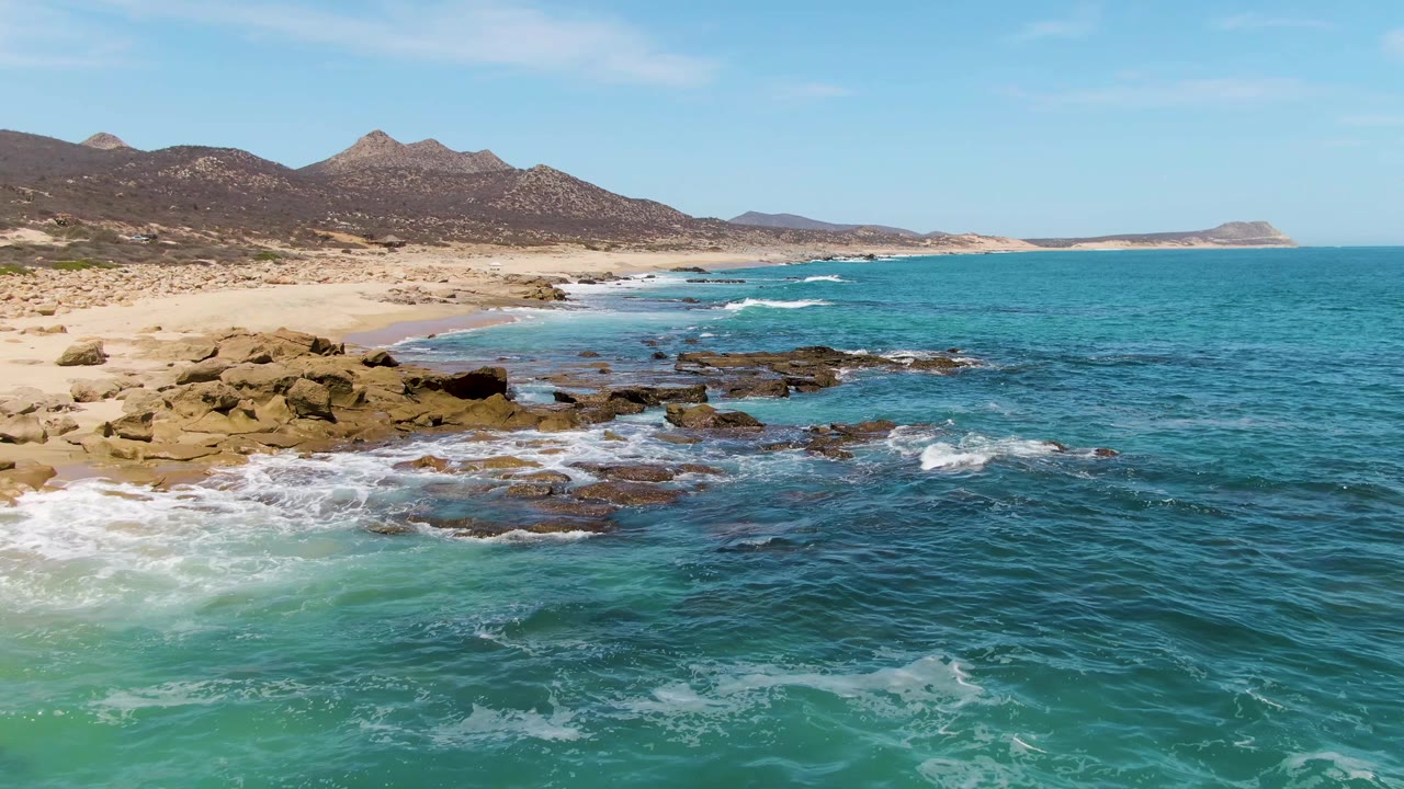 White surf breaking over shore rocks beside a sandy beach.