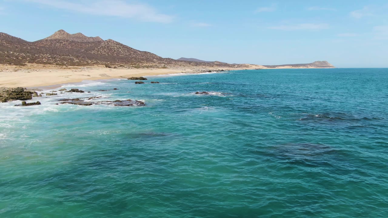 Surf washing along a sandy beach with rocks and mountains behind