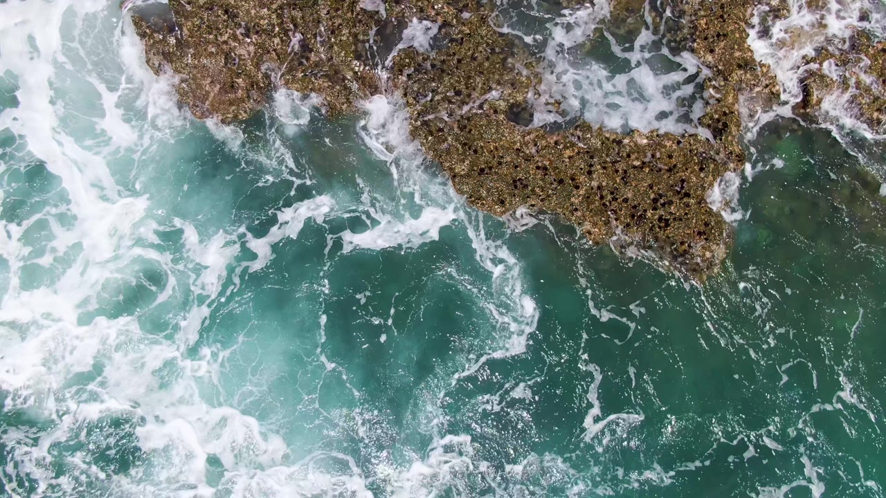 Overhead turquoise ocean waves breaking around brown rocks