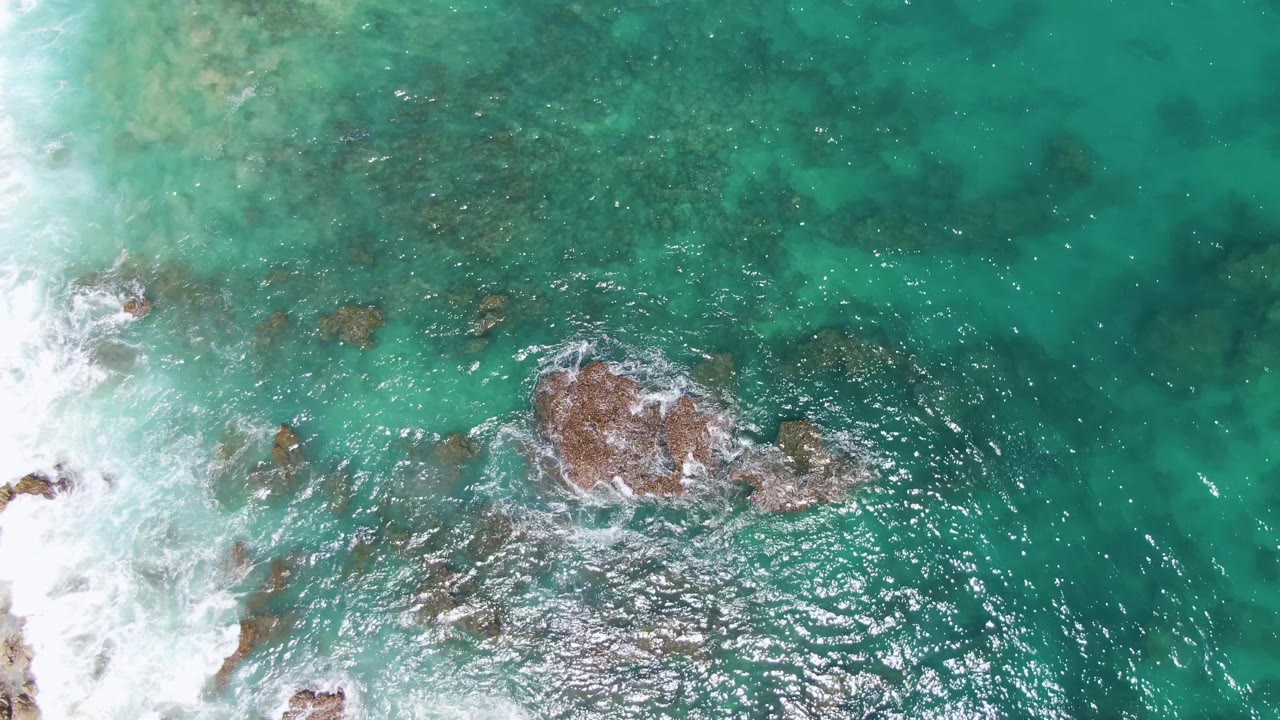 Aerial view of surf, rocks, and clear green ocean water