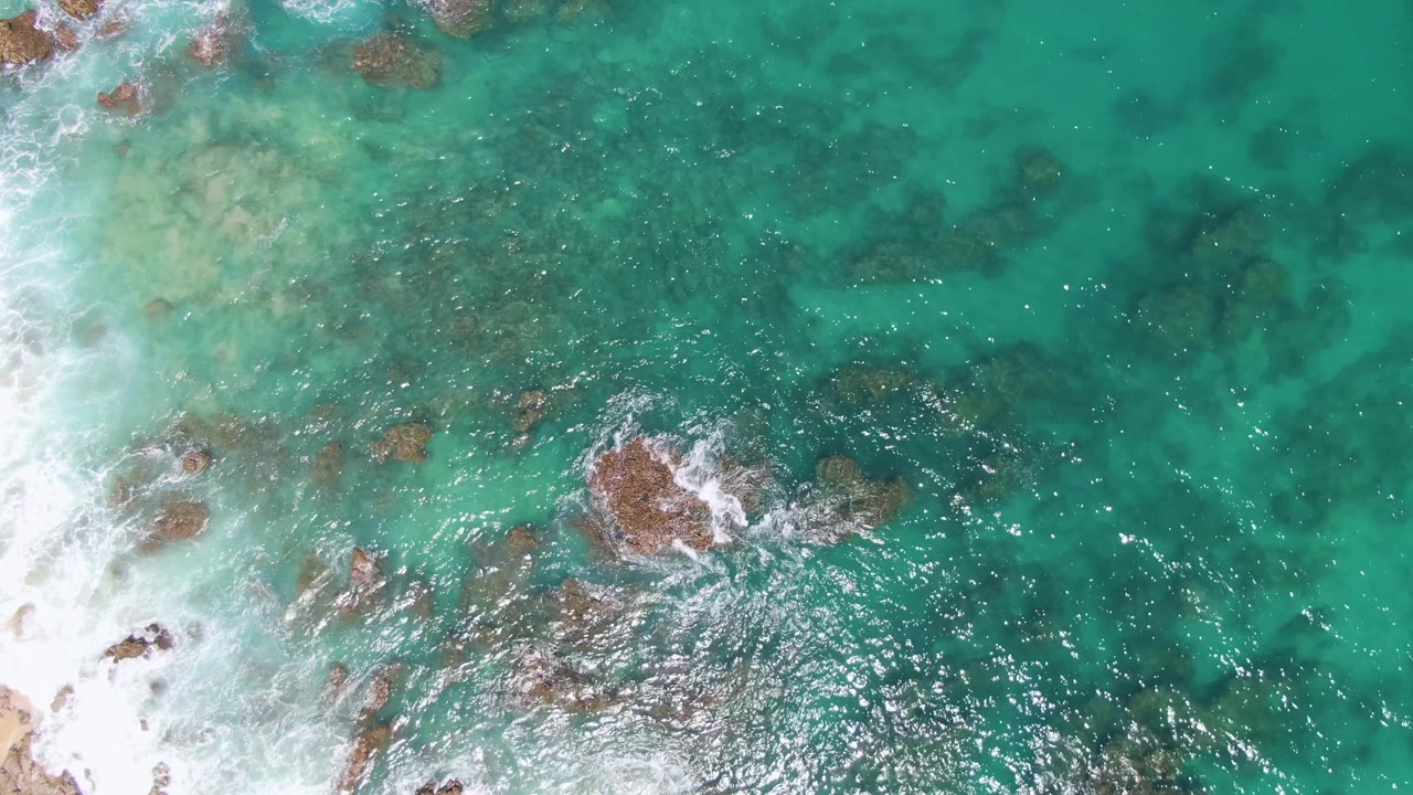 Overhead turquoise ocean with rocks and white surf foam