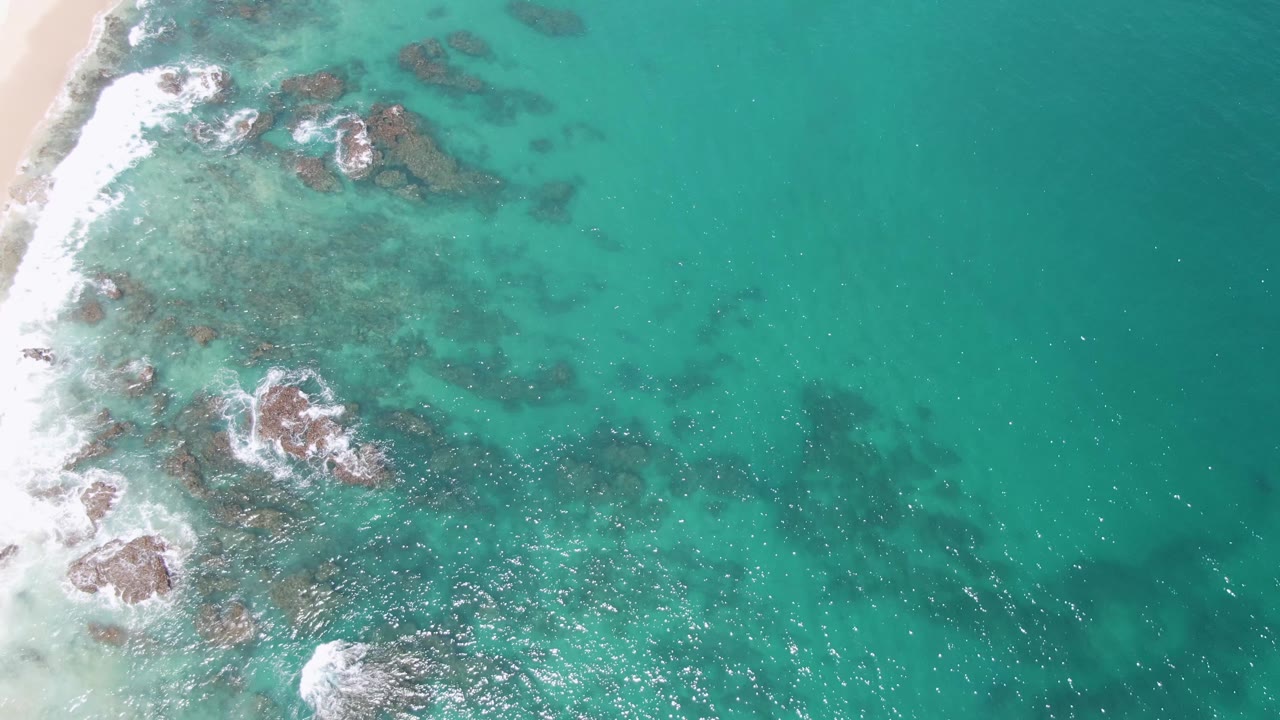 Beach edge and underwater rocks beneath clear turquoise surf