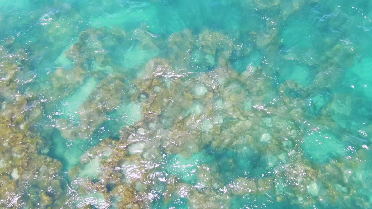 A rocky underwater patch sits beneath shallow turquoise water at Buzzards Beach, Baja California Sur, with scattered pale stones and no visible people.
