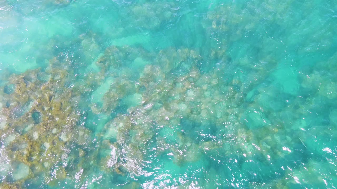 Overhead turquoise water with submerged rocks and surface ripples.
