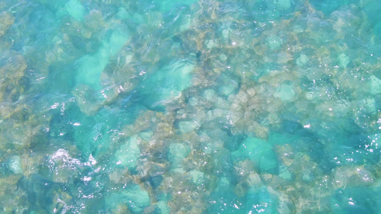 Overhead view of clear turquoise water at Buzzards Beach with submerged rocks visible through rippled surface light and no visible people.