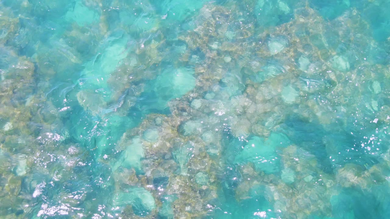 Clear shallow ocean water at Buzzards Beach shows pale and darker underwater rocks beneath shifting reflections, with no visible people.