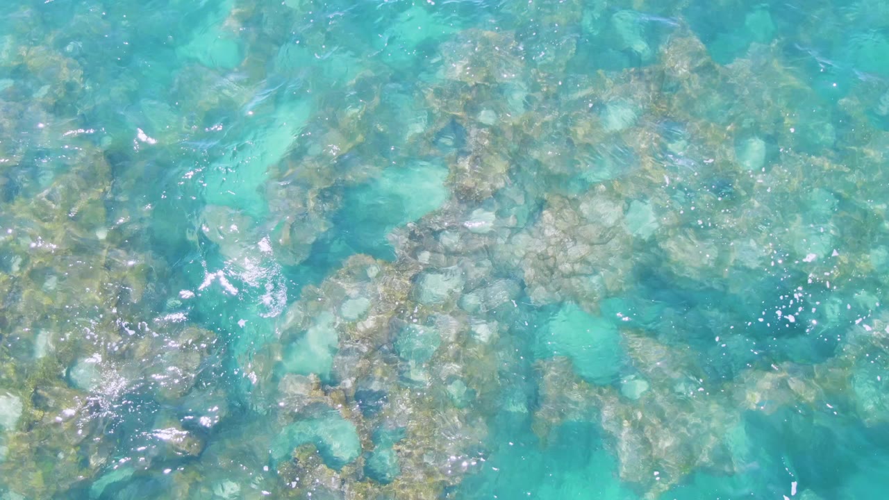 Turquoise surface ripples pass over clustered submerged rocks at Buzzards Beach, with small bright highlights and no visible people.