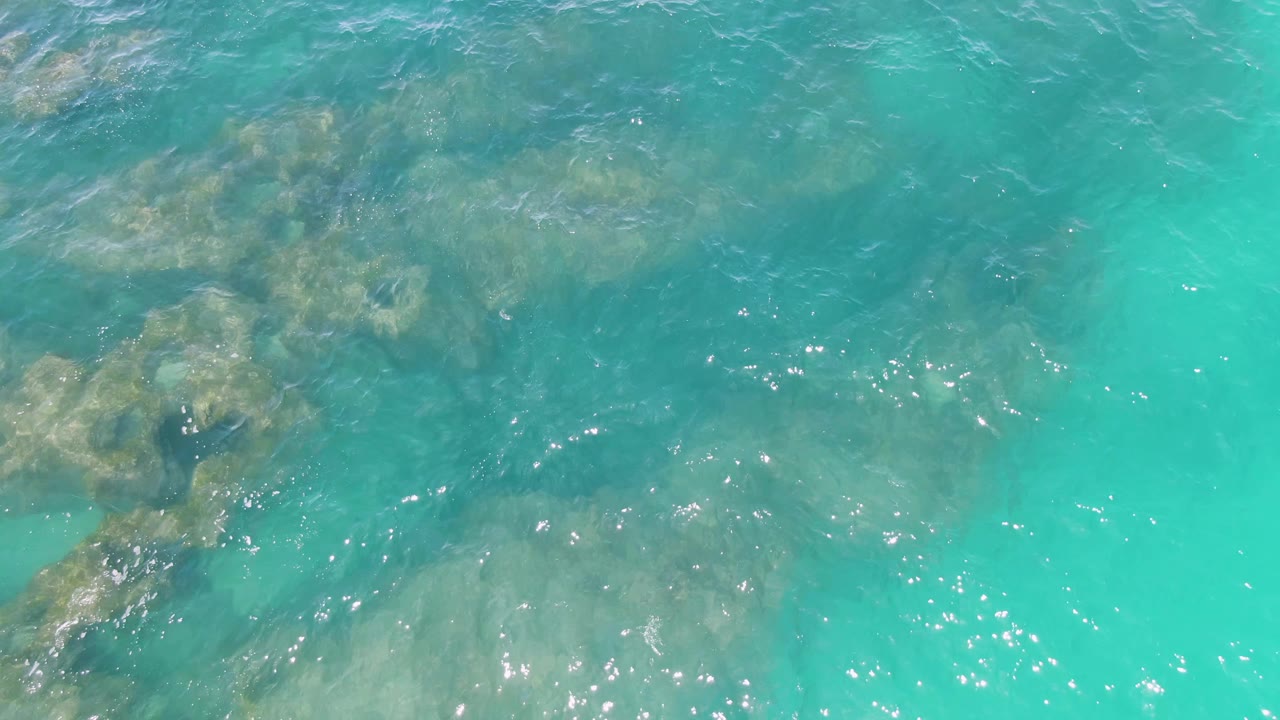 Clear turquoise water at Buzzards Beach, Baja California Sur, with submerged rock patches under ripples and no visible people.