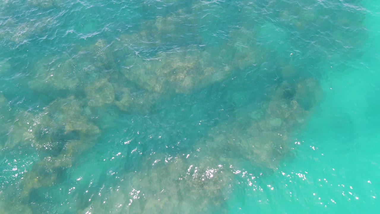 Clear aqua water with submerged rocks on the left and ripples across the surface.