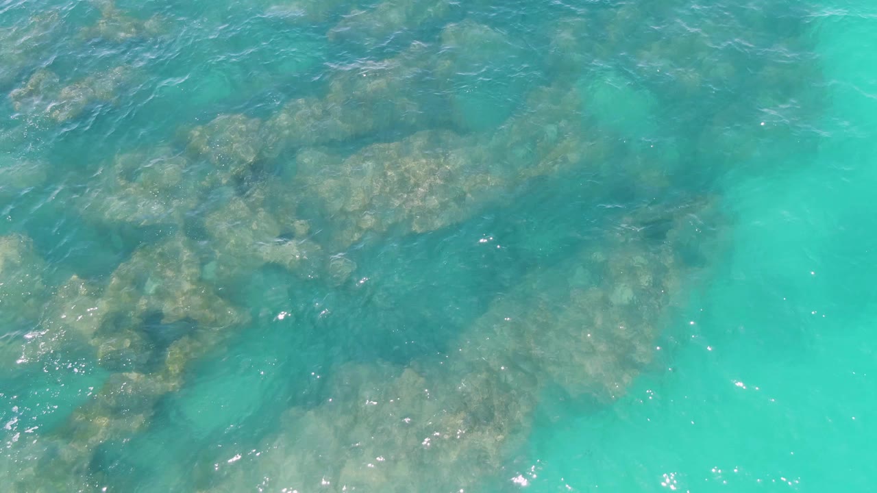 Overhead view of clear turquoise water at Buzzards Beach showing submerged rocks, pale sand, small surface ripples, and no visible people.