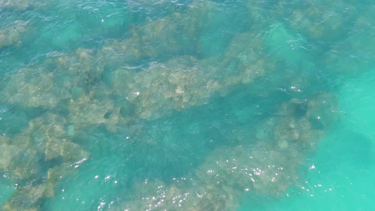 Clear water at Buzzards Beach passes over uneven submerged rocks, with scattered sun glints near the lower edge and no visible people.