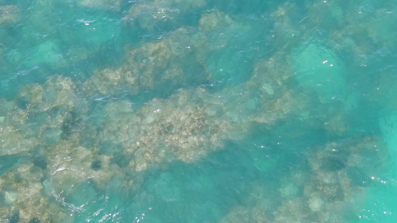 Sunlit ripples cross clear turquoise water at Buzzards Beach, Baja California Sur, revealing a clustered rocky seabed beneath the surface and no visible people.