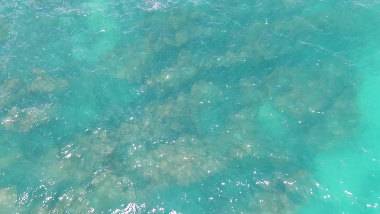 Overhead view of clear turquoise water at Buzzards Beach with submerged rocks visible beneath ripples and no visible people.